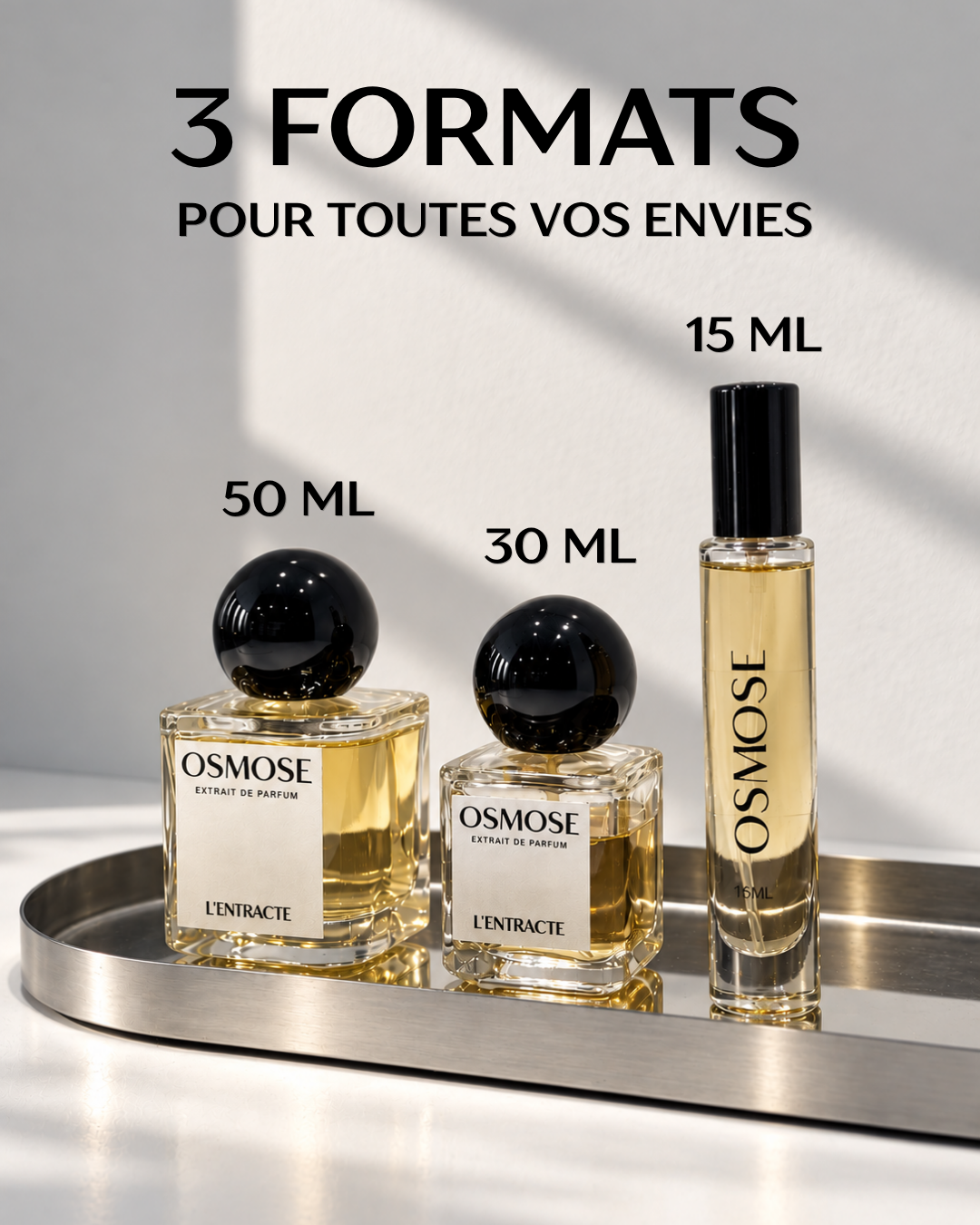 Three bottles of L’AIMANT fragrance vanillée in 50 ml, 30 ml, and 15 ml sizes displayed on a metal tray, with text above indicating the eau de parfum is available in three formats.