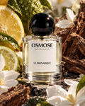 A bottle of LE MONARQUE Osmose eau de parfum with a round black cap, surrounded by citrus slices, bark, and white flowers.